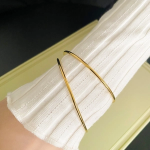 Detail of minimalist gold-plated crossover cuff bracelet worn over white knit sleeve