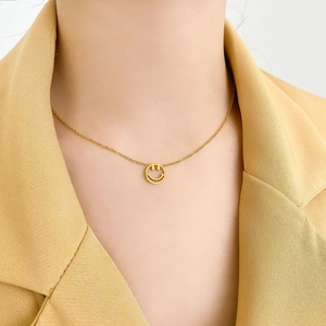 Collier élégant doré avec pendentif smiley porté par un mannequin en veste jaune