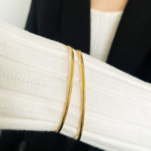 Close-up of minimalist gold plated stainless steel bangles worn over white knit sleeve
