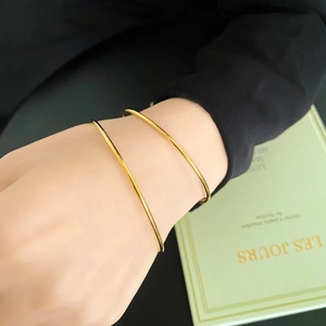 Minimalist stackable gold titanium bangles worn by model against a dark background