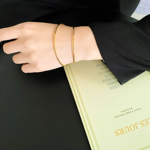 Close-up of minimalist gold-plated bangle worn on wrist against a dark backdrop