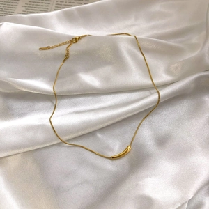 Detail of a minimalist gold curved tube pendant on a sleek snake chain over white silk