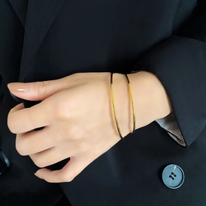 Close-up of minimalist gold-plated titanium steel bangle set on a black blazer sleeve