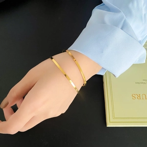 Close-up of minimalist gold plated stainless steel bangles worn with a blue shirt