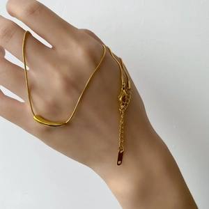 Detail of gold snake chain necklace with curved tube pendant worn by hand model
