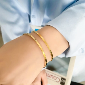 Detailed view of two polished gold-plated stainless steel bangles on a wrist