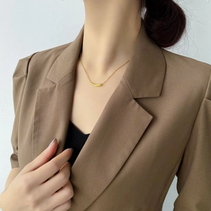 Close-up of minimalist gold curved tube pendant on a snake chain worn with a blazer