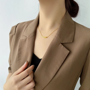 Close-up of a gold curved tube pendant necklace on a model wearing a brown blazer