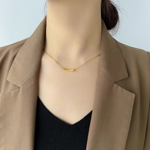 Minimalist gold snake chain necklace with curved smile pendant worn with a blazer