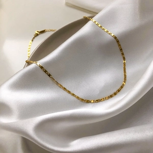 Gros plan détaillé du collier à maillons géométriques dorés sur fond de soie blanche