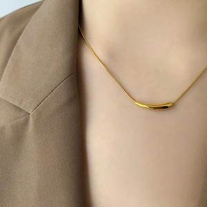 Close-up of minimalist gold snake chain necklace with curved smile tube on a brown blazer