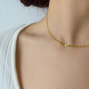Détail d'un collier chaîne à maillons nez de cochon doré sur un mannequin en tricot blanc