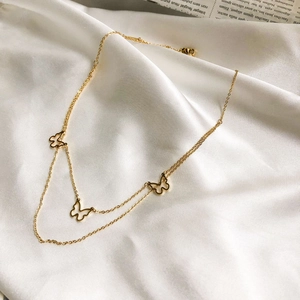 Detailed view of a gold double-layer butterfly necklace on a white silk background
