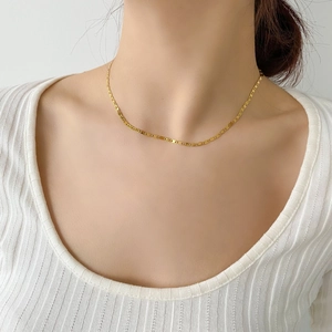 Détail d'un collier chaîne marinière dorée sur un col de chemise blanc côtelé