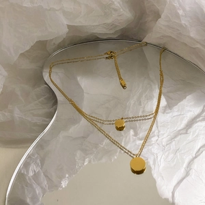 Artistic detail of gold double-layer necklace with circular pendants on wave mirror