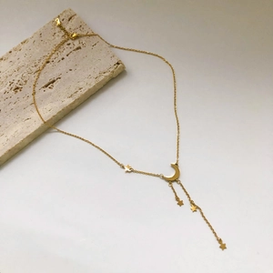 Collier pampille lune et étoile dorée avec chaîne réglable sur fond de pierre beige