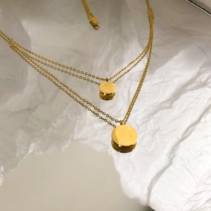 Minimalist double layer gold necklace with circular pendant on a white textured background