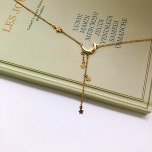Détail d'un collier en Y doré avec breloques lune et étoiles sur un carnet vert