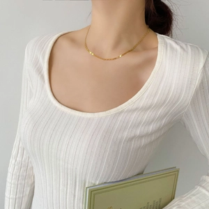 Détail d'un collier plat doré minimaliste porté par un mannequin en pull en maille blanc