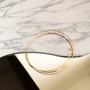 Minimalist multi-layered gold wire spring bracelet with delicate metal beads on marble