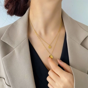 Double-layer gold necklace with two round pendants worn over a blazer for commute style