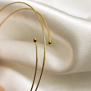 Close-up of a minimalist gold spring bracelet featuring small spherical ball ends on white silk