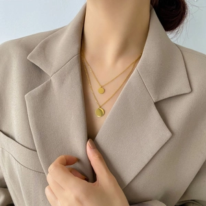 Close-up of minimalist layered gold necklace with two polished round pendants on model