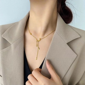 Gros plan du collier à pampilles lune et étoile dorées porté par un mannequin en blazer