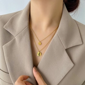 Close-up of a double-layered gold necklace with two round pendants on a model