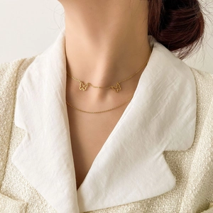 Detail of a gold double-layer butterfly necklace worn over a white elegant jacket