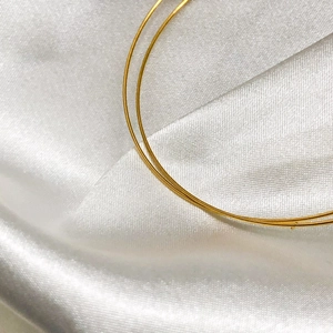 Close-up of a minimalist golden spring bracelet on a soft white silk background texture