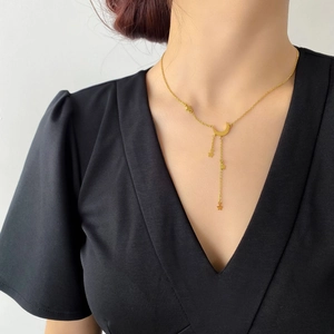 Gros plan d'un collier doré à pampilles étoile et lune porté par un mannequin sur du noir