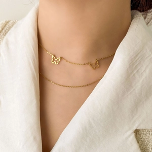 Detail of a layered golden necklace featuring two delicate hollow butterfly charms on a model