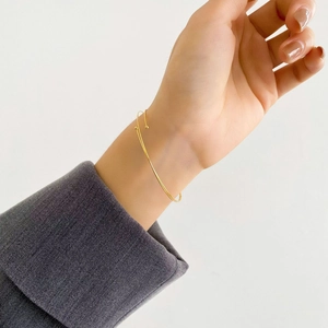 Detail of minimalist thin gold spring bracelet with small ball ends on woman wrist
