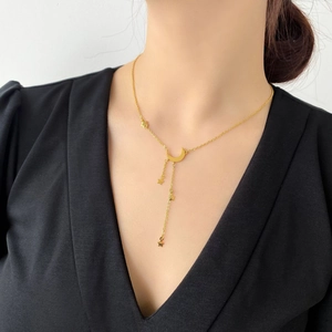Détail du collier à pampilles étoile et lune dorées sur mannequin avec col en V noir