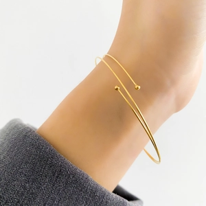 Detail of minimalist gold double-layered wire bracelet with ball ends on female wrist