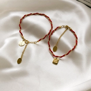 Close-up of red braided bracelets with gold 'Xi' and 'Good Luck' charms on white silk