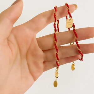 Red braided cord bracelet with gold beads and Good Luck square charm in hand