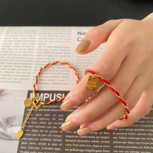 Red cord bracelet with gold Good Luck tag and beads on a vintage newspaper background