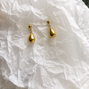 Macro detail of golden teardrop pendant earrings with polished metallic mirror finish