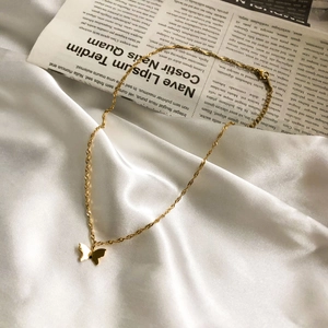 Collier papillon doré minimaliste avec chaîne torsadée sur fond de satin blanc