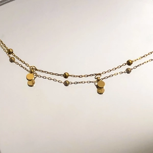 Detailed close-up of double-layer gold chain with small round beads and disc pendants