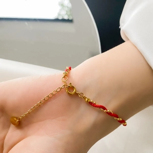 Detail of red braided bracelet with gold beads and lobster clasp on female wrist