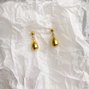 Detailed view of gold teardrop earrings with polished finish on wrinkled paper background