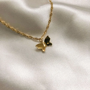 Détail d'un pendentif papillon doré sur une chaîne torsadée en soie blanche