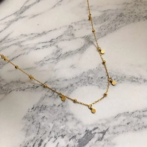 Close-up of a gold stainless steel necklace with small beads and polished round pendants