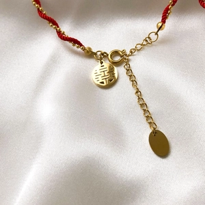 Close-up of red braided bracelet with golden Xi character charm and lobster clasp detail