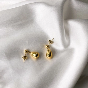 Polished gold teardrop earrings displayed on elegant white silk fabric background