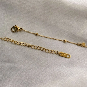 Close-up of 18k gold chain with lobster clasp and round bead detail on white silk