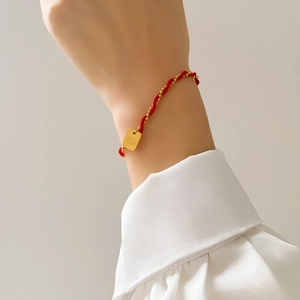 Macro shot of red braided rope bracelet featuring a gold square Good Luck charm on wrist